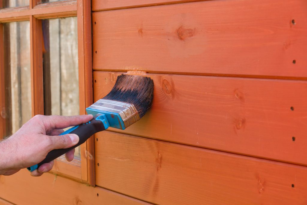 painting a shed orange with a wide brush