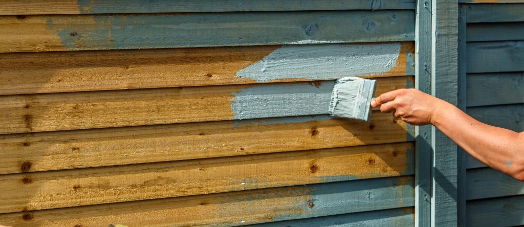 man's hand painting wooden Fence with a brush in sage green colour