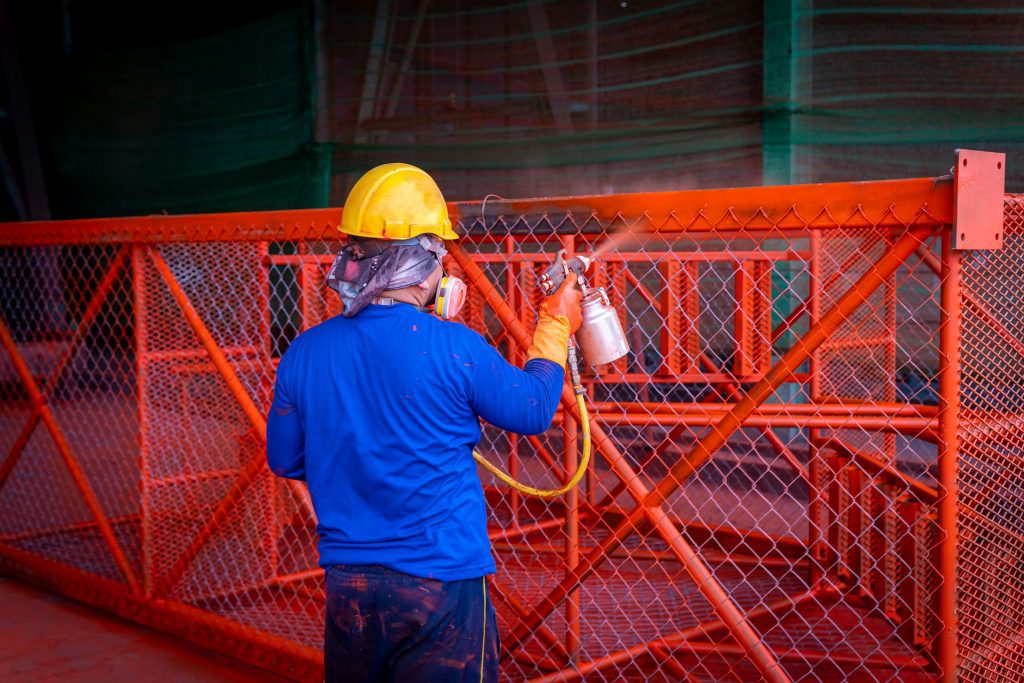 A man spraying a metal grate with orange paint